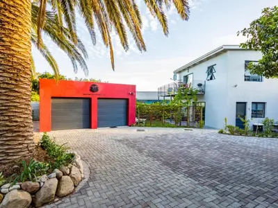 a red garage with a white building and a palm tree at Two Palm House - Vermont Hermanus in Hermanus