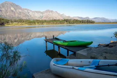 two canoes on a dock on a lake with mountains at Wild Olive House at Bartholomeus Klip in Hermon