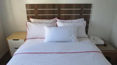 a white bed with white pillows and a wooden headboard at Galaxy Sleep And Go Rooms Goodwood in Cape Town