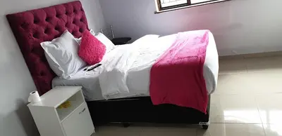 a bed with a red head board with pink pillows at PEACE LODGE in Cape Town