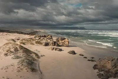 a beach with rocks and the ocean on a cloudy day at TnT on Main in Hermanus