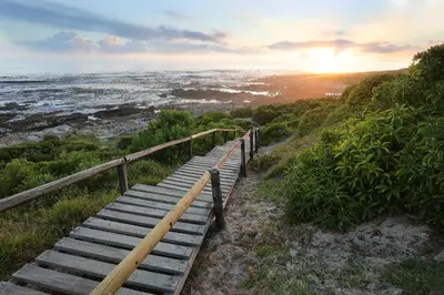 a wooden staircase leading to the ocean at sunset at Oak on Main in Hermanus