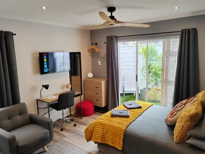 a bedroom with a bed and a chair and a television at Leafy Retreat Kenridge Trendy in Durbanville