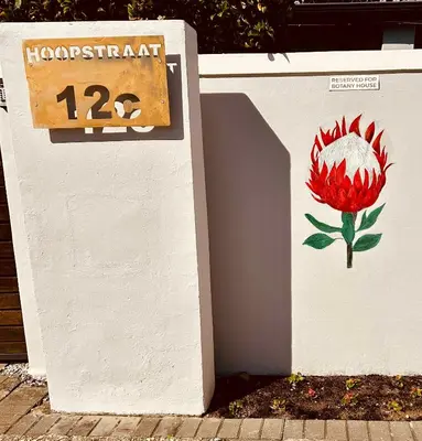 a sign on a wall with a flower painted on it at Botany House, in the heart of Hermanus in Hermanus