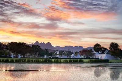 a sunset over a lake with houses and mountains at Vergenoegd Löw Boutique Hotel & Spa in Somerset West