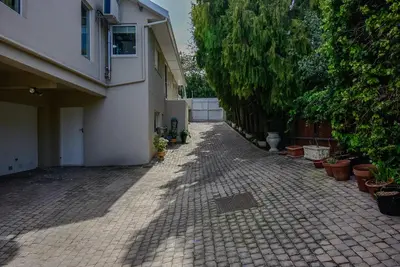 a brick driveway next to a white building with plants at Garden- Pool flat with Solar Electricity in Somerset West