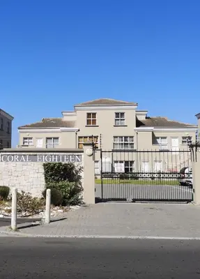 a building with a sign in front of a fence at Blouberg Beach Luxury Apartment in Cape Town