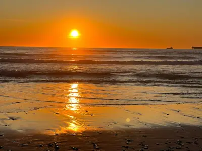 a sunset on the beach with the sun setting at Cowrie Cottage Self Catering in Cape Town