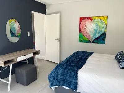 a bedroom with a bed with a heart painting on the wall at Cowrie Cottage Self Catering in Cape Town