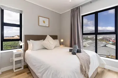 a bedroom with a white bed with large windows at Burmeister 401 - 2 Bedroom Apartment across from Ocean - Onsite Parking in Cape Town