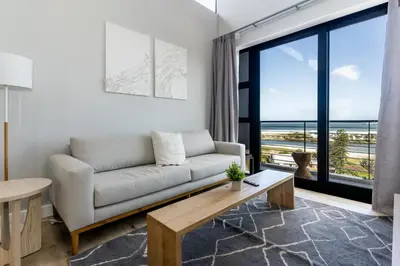 a living room with a couch and a large window at Burmeister 607 - Top Floor Corner 2 Bedroom Apartment with Sea and Lagoon Views - Onsite Parking in Cape Town