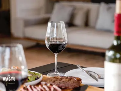 a glass of wine sitting on a table with a plate of food at Wagyu Mountain Lodge in Paarl
