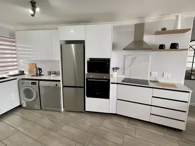 a kitchen with white cabinets and a washer and dryer at Luxurious 2-bedroom beach apartment with a view! in Bloubergstrand