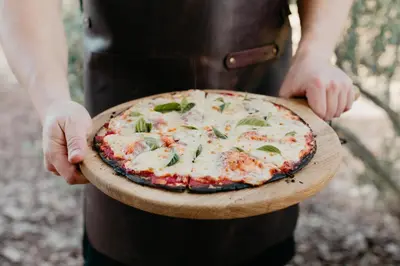 a person holding a pizza on a wooden plate at untether on Olive View in Wellington