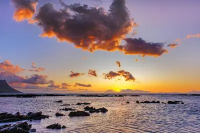 a sunset on a beach with rocks in the water at Villa Kyma in Gordonʼs Bay