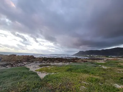 a beach with the ocean and a cloudy sky at Adorable 2 Bedroom Cottage with spacious veranda in Hermanus
