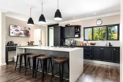 a kitchen with black cabinets and bar stools at Luxury Stellenbosch Villa in Stellenbosch
