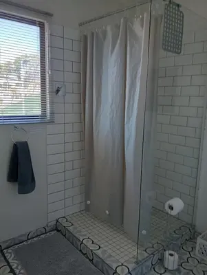 a shower with a glass shower curtain in a bathroom at The Wee Hoose in Strand