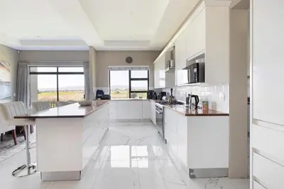 a white kitchen with white cabinets and a table at On 8th Green Worthing Villa in Cape Town