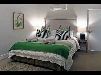 a bedroom with a large bed with green sheets and pillows at The Village Cottage in Franschhoek