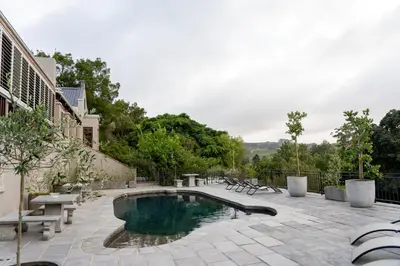 a swimming pool with benches and a patio with at Avemore Olive Apartment - full Backup power in Stellenbosch
