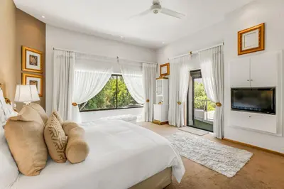 a white bedroom with a large bed and a tv at Erinvale Luxury Villa in Cape Town