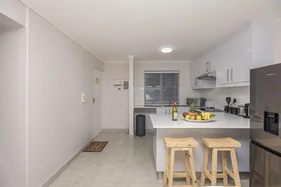 a white kitchen with two stools and a counter at Blouberg Pearl in Cape Town