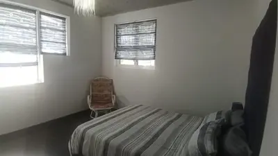 a bedroom with a bed and a chair and two windows at Whalers Retreat in Bettyʼs Bay