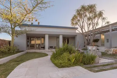 a white house with palm trees and a patio at Benguela Cove - Oceans Away in Hermanus