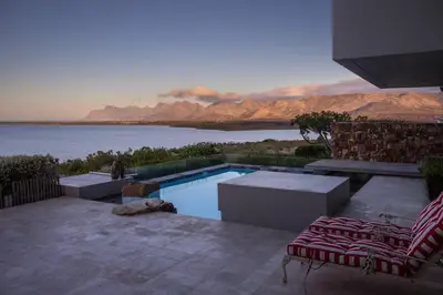 a swimming pool with two chairs and a view of the water at Benguela Cove - Oceans Away in Hermanus