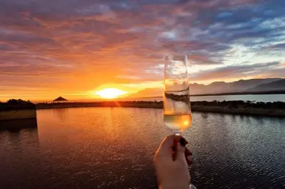 a person holding a glass in front of a sunset at Benguela Cove - Coastal Retreat in Hermanus