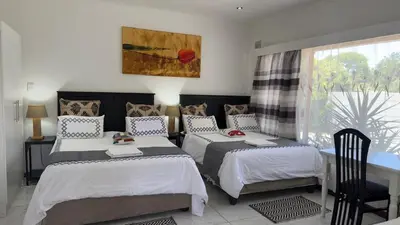 a bedroom with two beds and a table and a window at MELJAA STAR Guesthouse in Cape Town