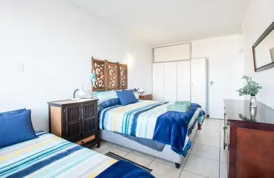 a bedroom with two beds and a dresser at Strand Apartment only 30 meters from beach in Cape Town