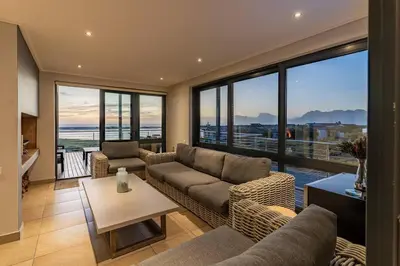 a living room with couches and a table and windows at Hermanus Beach House at CShine in Hermanus