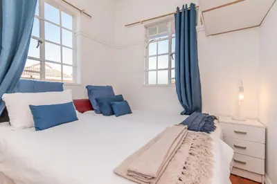 a white bedroom with blue curtains and a bed at Secure and Modern 2Bed Apartment in Cape Towns Charming Rondebosch in Cape Town