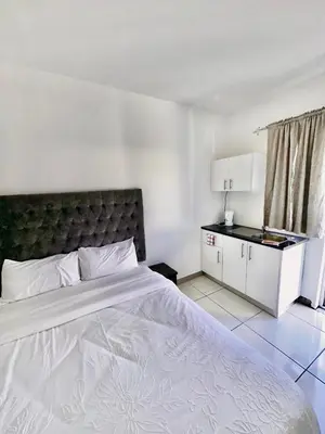 a bedroom with a large white bed and a kitchen at Beatrice Guesthouse in Cape Town