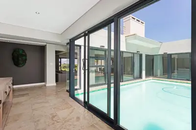 an indoor swimming pool in a house with glass walls at Sunset Kite & Golf Villa in Cape Town
