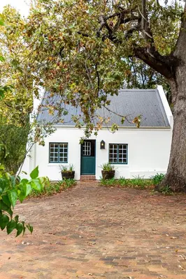 a white house with a green door and a tree at Plaisir Estate Accommodation in Simondium