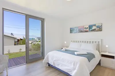 a white bedroom with a bed and a large window at Suidersee-Voelklip in Hermanus