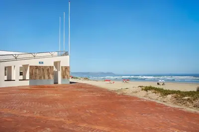 a building on the beach with the ocean in the background at Suidersee-Voelklip in Hermanus