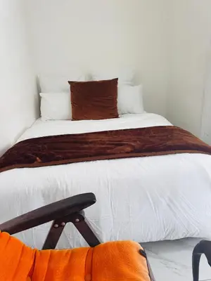 a bedroom with a bed with white sheets and a chair at Mila Lodge 2 in Cape Town