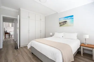 a white bedroom with a large bed and a table at Wegbreek in Hermanus