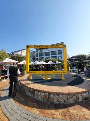 a man standing in front of a yellow sign at *Self-Check in - Whale Watching Paradise -Central* in Hermanus