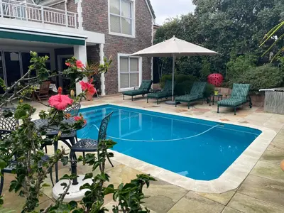 a swimming pool with chairs and an umbrella at De Blauwvoet - Meerkat (Sunset Beach) in Cape Town