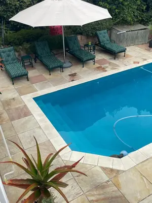 a swimming pool with green chairs and an umbrella at De Blauwvoet - Dolfyn (Sunset Beach) in Cape Town