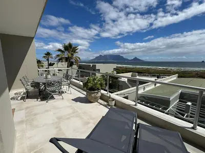 a balcony with chairs and a table and the ocean at Dolphin Beach beachfront apartment, 3 bedroom-6 persons in Cape Town