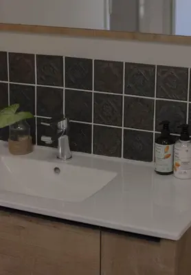 a bathroom counter with a white sink and black tiles at Three Streams Cottages in Franschhoek