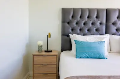 a bed with a blue pillow next to a night stand at Portico 1006 Beachfront Apartment with Panoramic Views in Cape Town