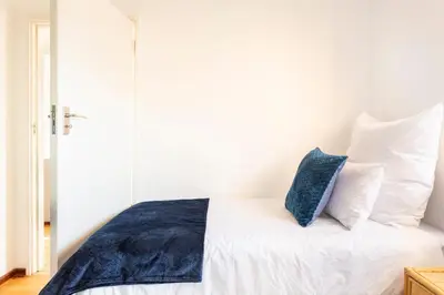 a bedroom with a white bed with a blue pillow at Innie Baai Beach House in Cape Town