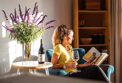 a woman sitting in a chair reading a book and a glass of wine at Luxury suite near Church Street in Stellenbosch